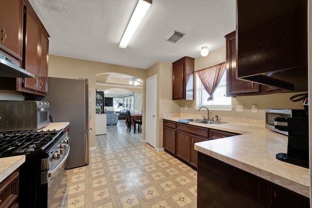 kitchen with visible vents, arched walkways, stainless steel appliances, light floors, and a sink
