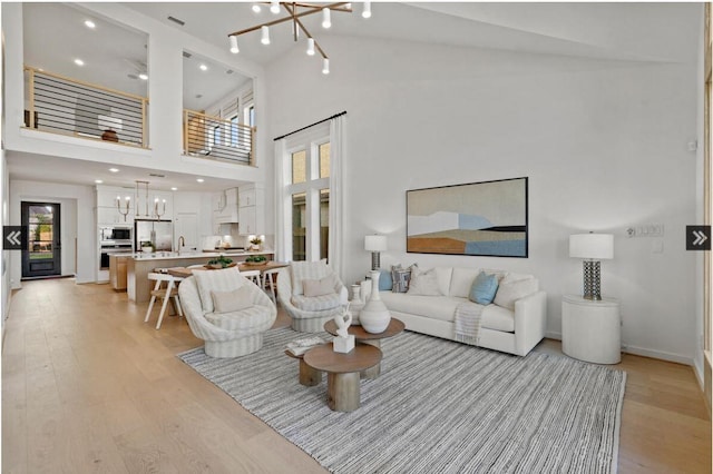 living area featuring light wood-style floors, high vaulted ceiling, baseboards, and an inviting chandelier