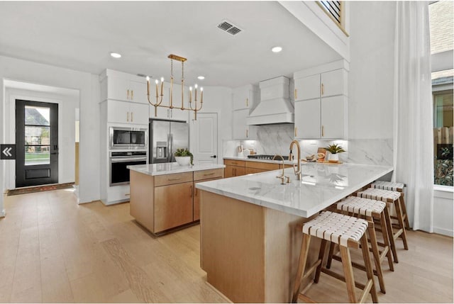 kitchen featuring light wood finished floors, visible vents, stainless steel appliances, premium range hood, and backsplash