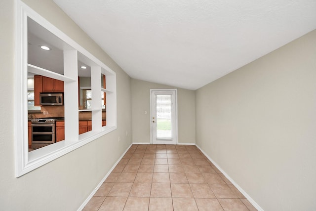 doorway featuring lofted ceiling, light tile patterned flooring, and baseboards