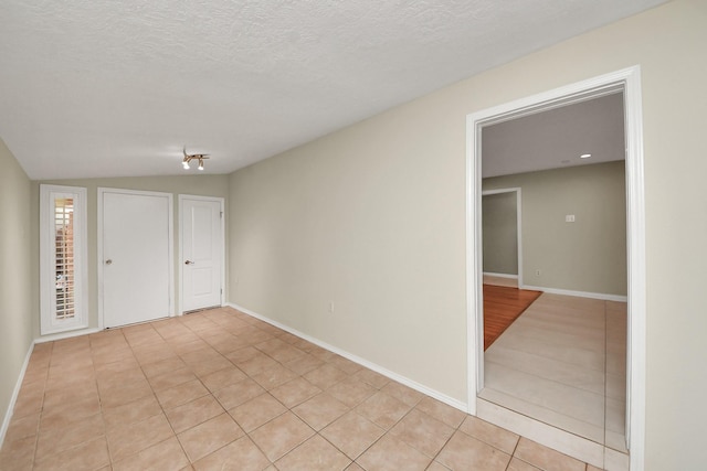 spare room featuring baseboards, vaulted ceiling, and a textured ceiling