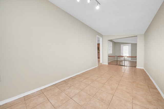 empty room with light tile patterned floors, baseboards, and rail lighting