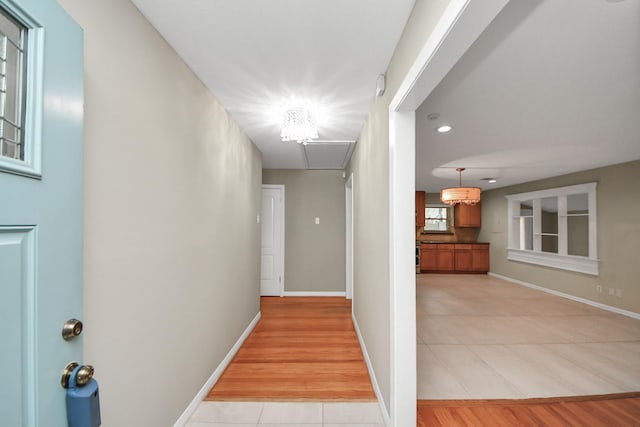 hall featuring light tile patterned floors, baseboards, and an inviting chandelier