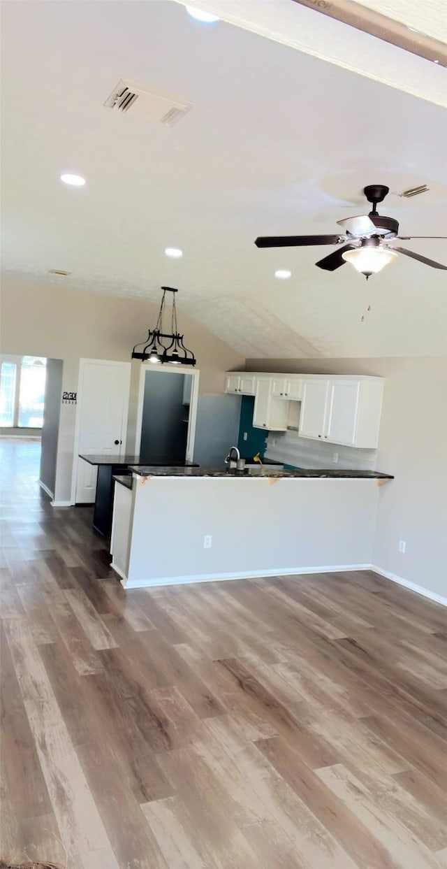 kitchen with visible vents, white cabinets, dark countertops, wood finished floors, and vaulted ceiling