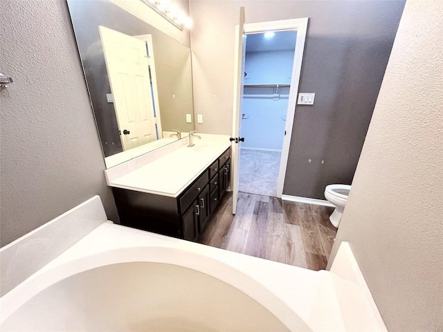 full bathroom featuring toilet, wood finished floors, a walk in closet, vanity, and a bath