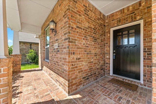 doorway to property featuring a porch and brick siding