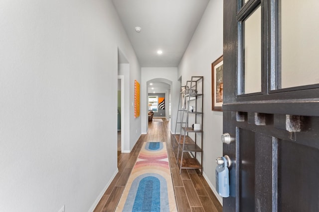 corridor with arched walkways, wood finish floors, and baseboards