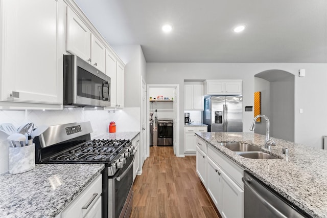 kitchen featuring arched walkways, stainless steel appliances, wood finished floors, a sink, and backsplash