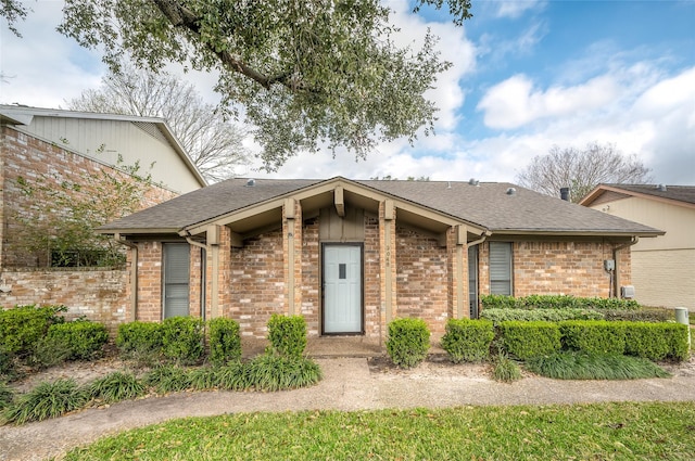 mid-century home featuring a shingled roof and brick siding