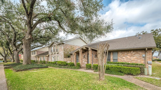 mid-century home with roof with shingles, a front yard, and brick siding