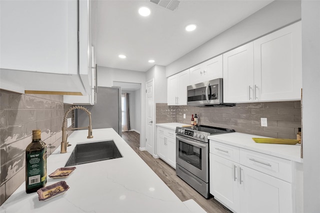 kitchen featuring stainless steel appliances, visible vents, light wood-style flooring, white cabinets, and a sink