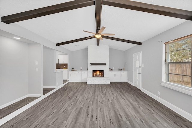 unfurnished living room with lofted ceiling with beams, a fireplace, baseboards, and wood finished floors