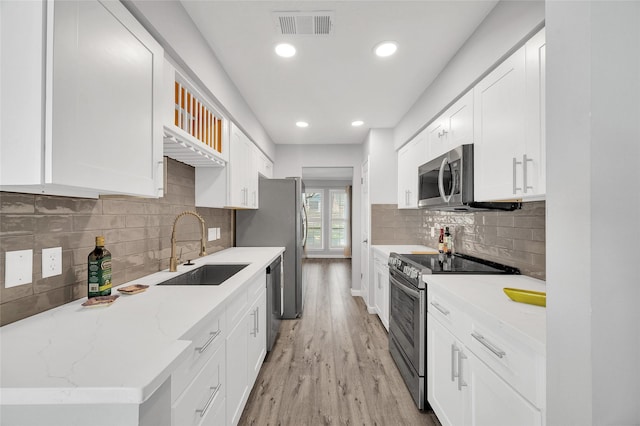 3048 Gessner Rd, Houston, TX 77080 - kitchen with appliances with stainless steel finishes, a sink, light wood finished floors, white cabinets, and decorative backsplash