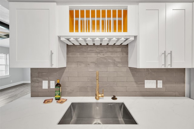 kitchen with light stone counters, white cabinets, a sink, and decorative backsplash