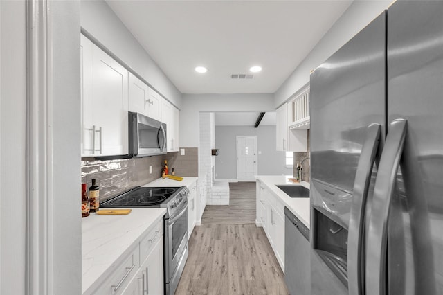 3048 Gessner Rd, Houston, TX 77080 - kitchen featuring stainless steel appliances, a sink, light wood-style flooring, decorative backsplash, and white cabinetry