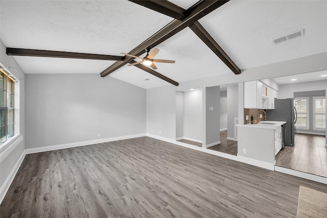 unfurnished living room with visible vents, a sink, baseboards, and wood finished floors