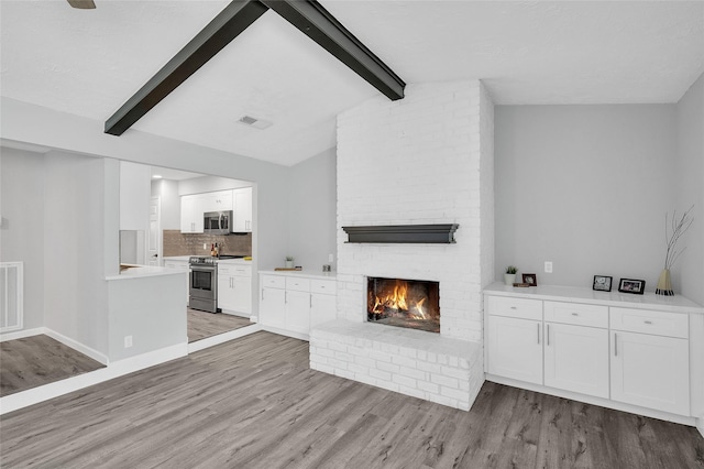 unfurnished living room with lofted ceiling with beams, light wood-style flooring, a brick fireplace, and visible vents