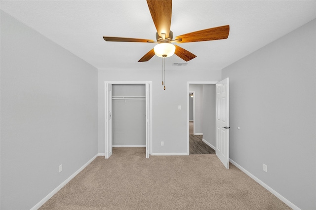 unfurnished bedroom featuring a closet, light colored carpet, visible vents, a ceiling fan, and baseboards