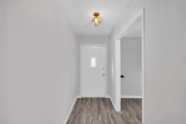 doorway to outside featuring a textured ceiling, light wood-style flooring, and baseboards