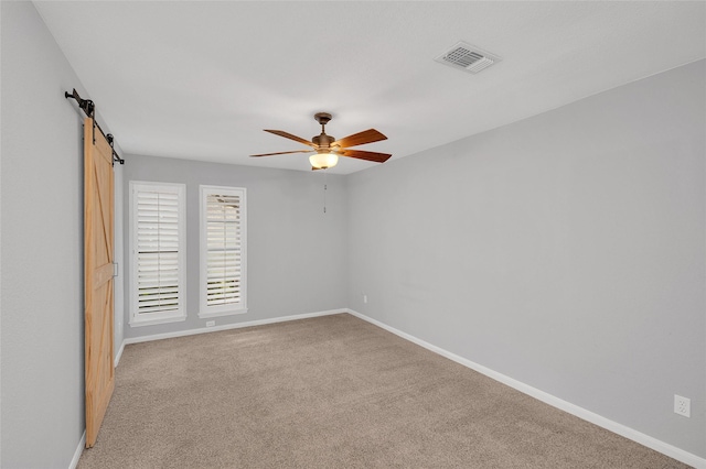 empty room with a barn door, baseboards, visible vents, a ceiling fan, and light colored carpet