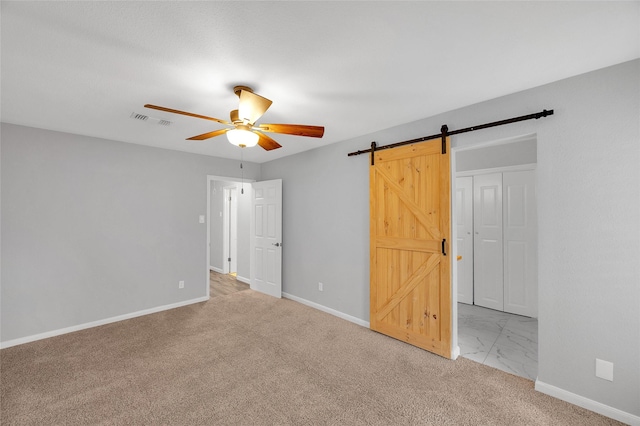 unfurnished bedroom with marble finish floor, a barn door, visible vents, and baseboards