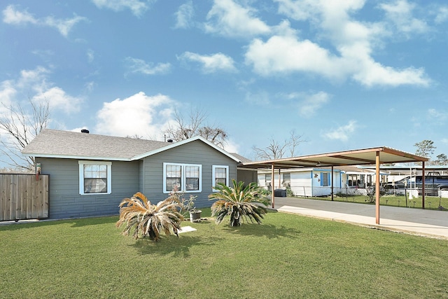 view of front of home with a shingled roof, fence, a carport, driveway, and a front lawn