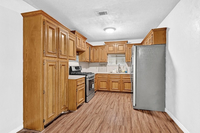 kitchen featuring light wood finished floors, light countertops, visible vents, appliances with stainless steel finishes, and a sink