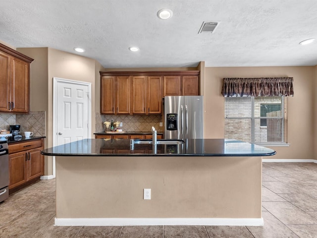 kitchen featuring a center island with sink, visible vents, brown cabinets, and stainless steel fridge with ice dispenser