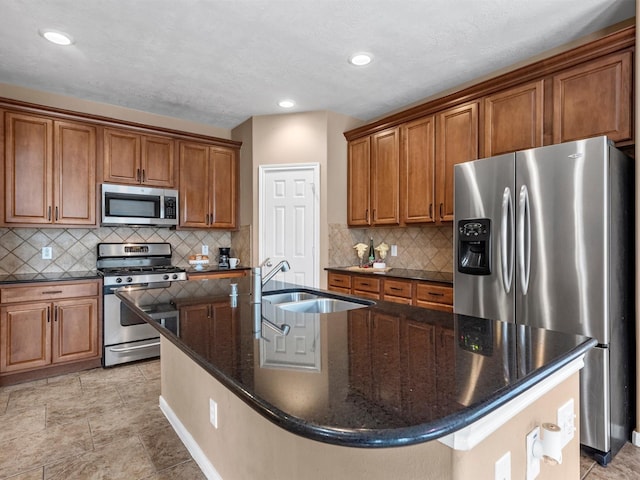 kitchen with an island with sink, brown cabinetry, stainless steel appliances, and a sink