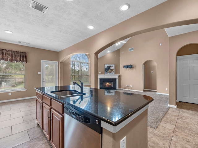 kitchen with a sink, visible vents, open floor plan, stainless steel dishwasher, and a glass covered fireplace