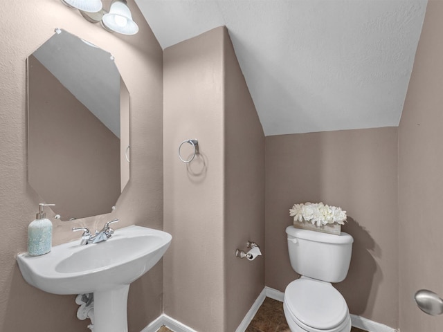 half bath with toilet, baseboards, vaulted ceiling, and a sink