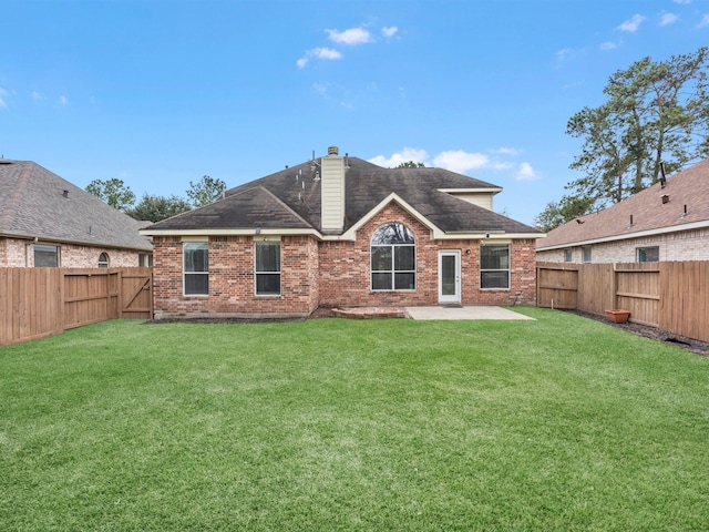 back of property featuring a chimney, brick siding, a yard, and a fenced backyard