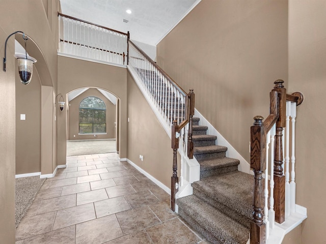 foyer featuring a towering ceiling, baseboards, arched walkways, and tile patterned floors