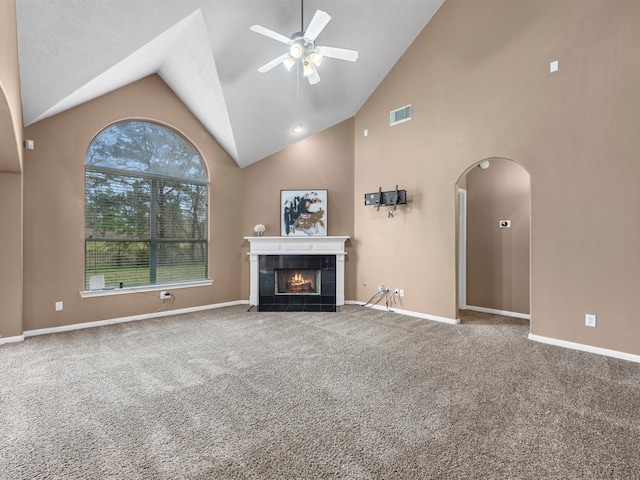 unfurnished living room with arched walkways, ceiling fan, carpet flooring, baseboards, and a tiled fireplace