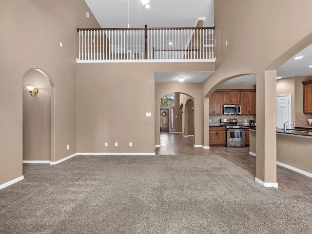 unfurnished living room with arched walkways, carpet, and baseboards