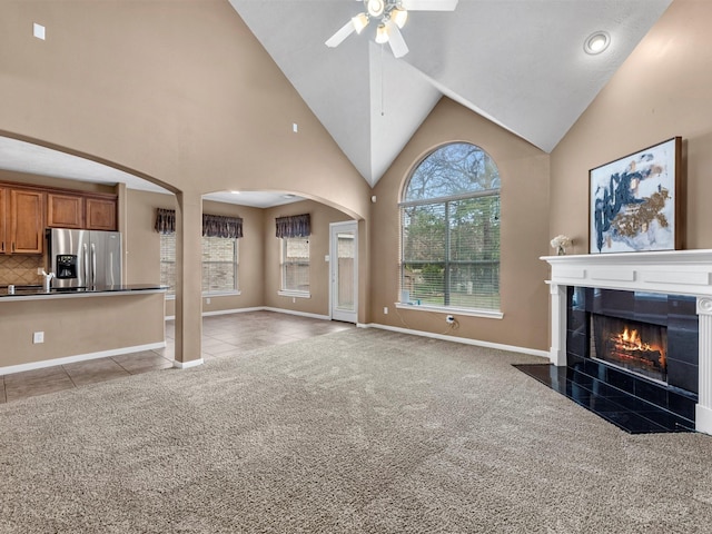 unfurnished living room with ceiling fan, light tile patterned floors, arched walkways, light carpet, and a tiled fireplace