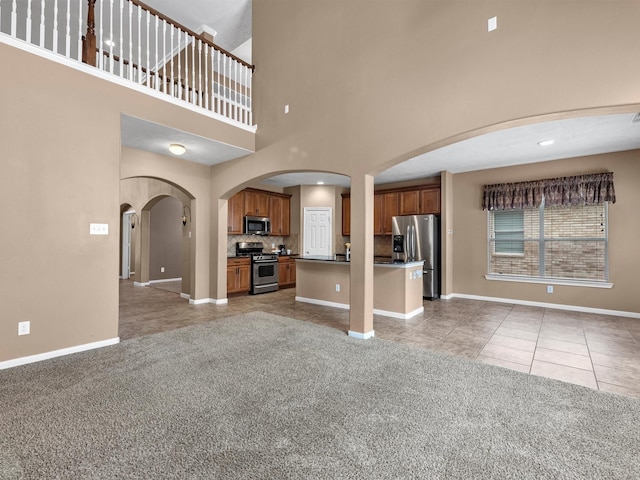 unfurnished living room featuring arched walkways, a towering ceiling, baseboards, and light tile patterned floors