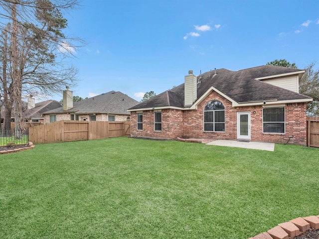 back of house with a lawn, a patio, a fenced backyard, a chimney, and brick siding