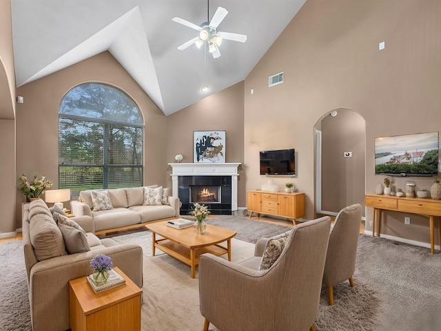 living room featuring arched walkways, ceiling fan, light colored carpet, visible vents, and a tiled fireplace