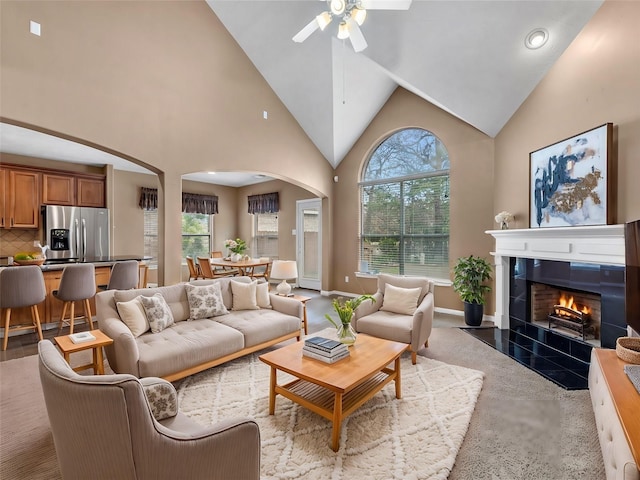 living room with a healthy amount of sunlight, high vaulted ceiling, arched walkways, and a tile fireplace