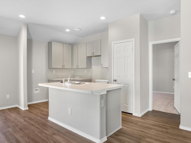 kitchen featuring a kitchen island with sink, a sink, visible vents, baseboards, and dark wood-style floors