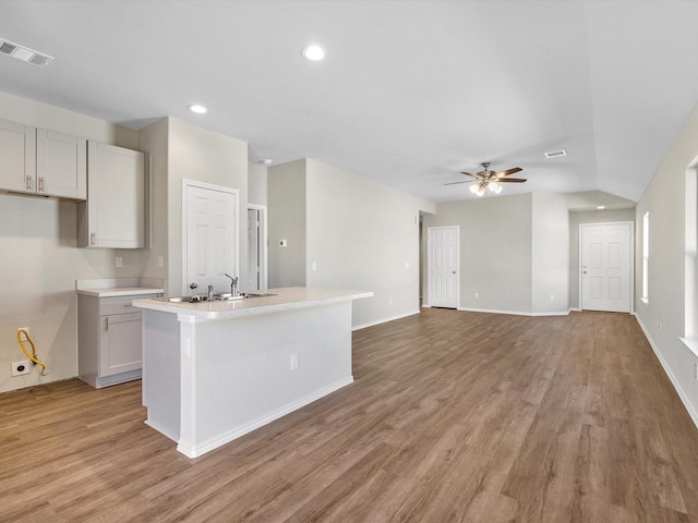 kitchen with light countertops, visible vents, a ceiling fan, an island with sink, and light wood-type flooring