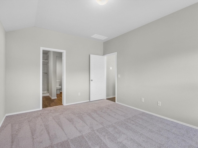 unfurnished bedroom featuring baseboards, visible vents, lofted ceiling, ensuite bath, and carpet flooring