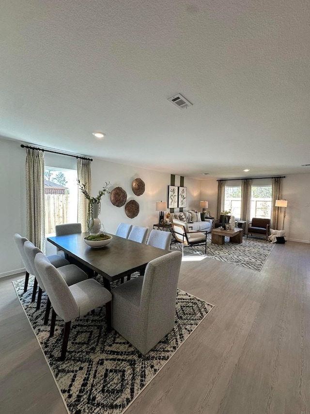 dining space with visible vents, a textured ceiling, baseboards, and wood finished floors