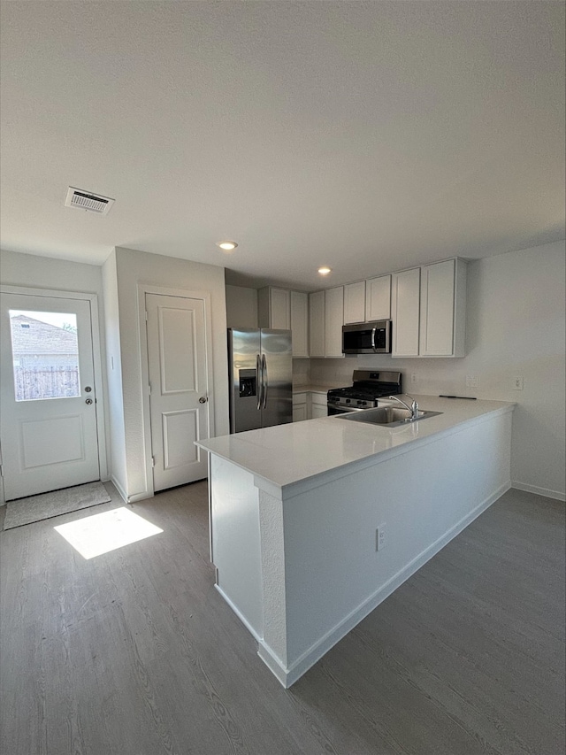 kitchen with baseboards, appliances with stainless steel finishes, wood finished floors, a peninsula, and light countertops