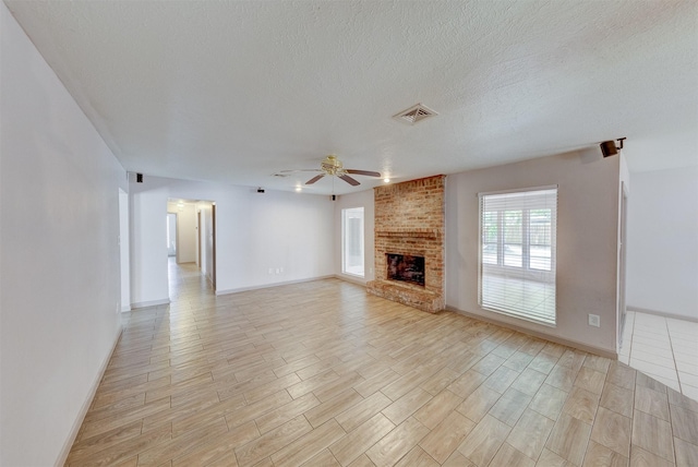 unfurnished living room with a fireplace, light wood finished floors, visible vents, ceiling fan, and a textured ceiling