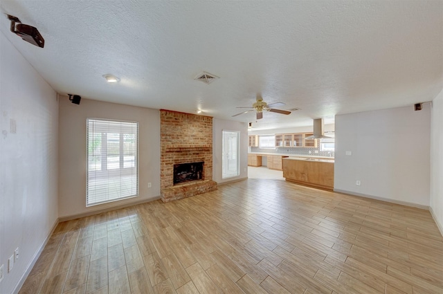 unfurnished living room featuring a brick fireplace, visible vents, ceiling fan, and light wood-style flooring