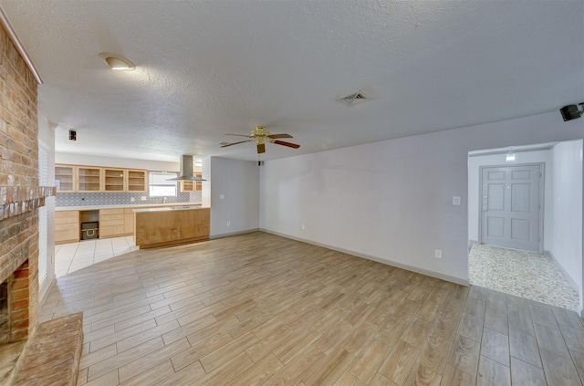 unfurnished living room featuring visible vents, a textured ceiling, light wood-style flooring, and a ceiling fan