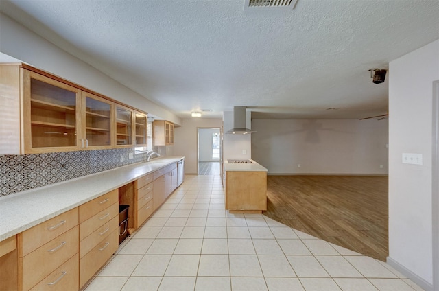 kitchen with decorative backsplash, open floor plan, light tile patterned flooring, a sink, and wall chimney exhaust hood