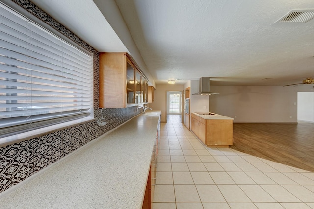 kitchen featuring visible vents, glass insert cabinets, open floor plan, a textured ceiling, and wall chimney range hood